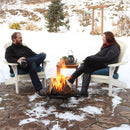 Two adults talking and sitting in adirondack chairs while the portable easy-folding fire pit burns a fire