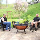 Woman and man sitting on black Adirondack chairs around a lit, copper-colored fire while the spark screen rests on the left-hand side.